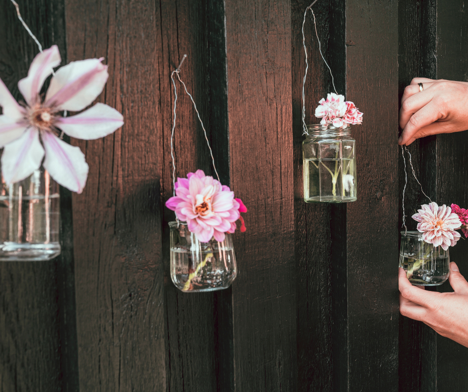 Glass jars upcycled into vases for 4 pink flowers hung on a brown wall Glass jars upcycled into vases for 4 pink flowers hung on a brown wall