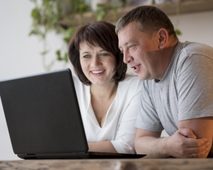 Grandparents on video call A woman and a man sit in front of a laptop, looking at the screen and smiling.