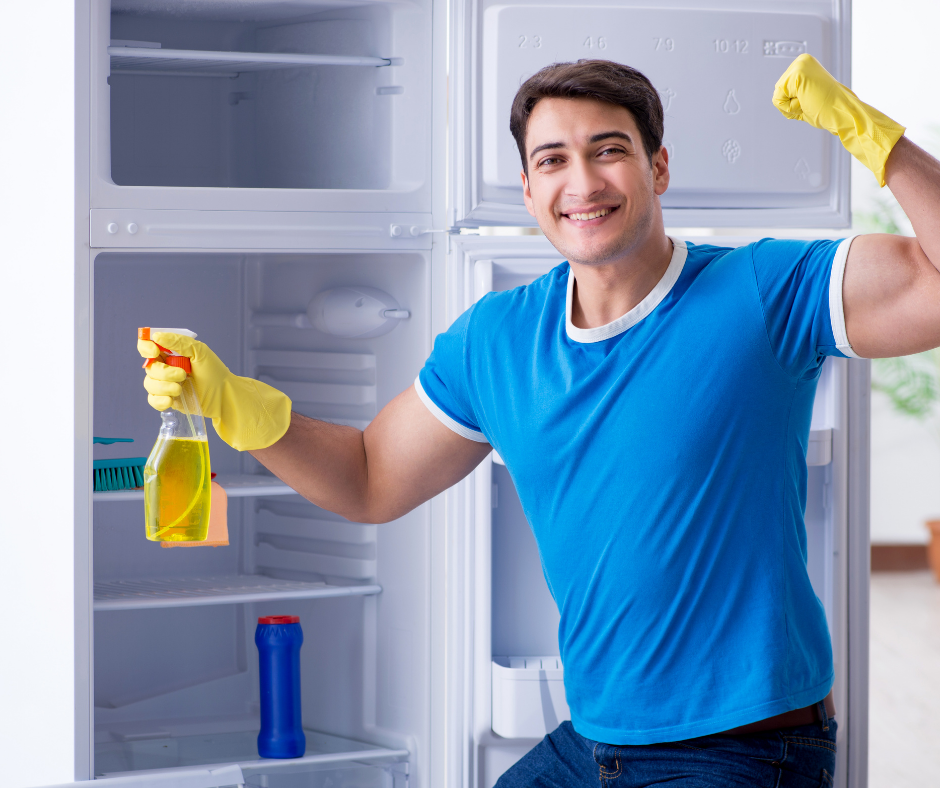 Man in a blue t-shirt with yellow gloves and a spray bottle cleaning a fridge Man in a blue t-shirt with yellow gloves and a spray bottle cleaning a fridge