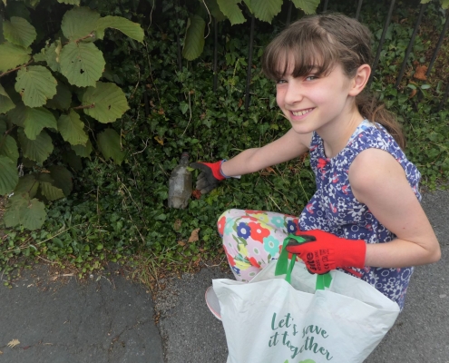 Girl picking up litter from a hedge wearing gloves