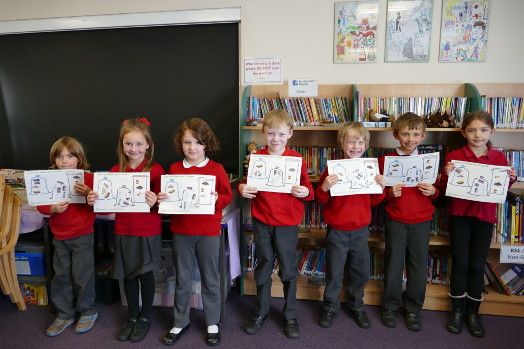 Children of St Johns, Totnes proudly displaying their work Line of children dressed in school uniform holding up pieces of paper