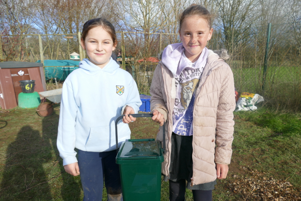Cornwood Primary School Two children holding a green compost bin standing in a school garden