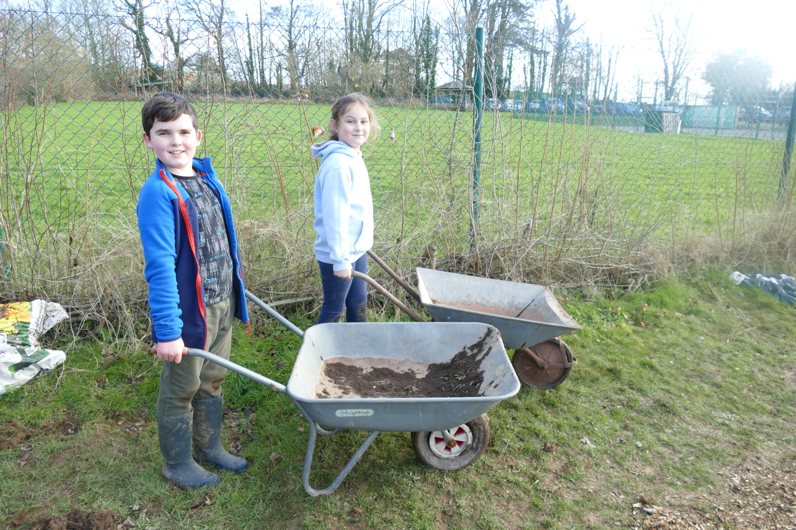 Two children push wheelbarrows, turned to look at camera