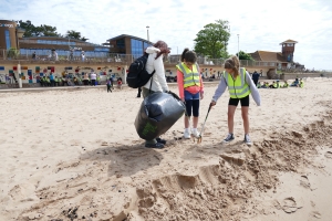 Woman and two children using litter pickers and a black bin bag to collect rubbish on a beach Woman and two children using litter pickers and a black bin bag to collect rubbish on a beach