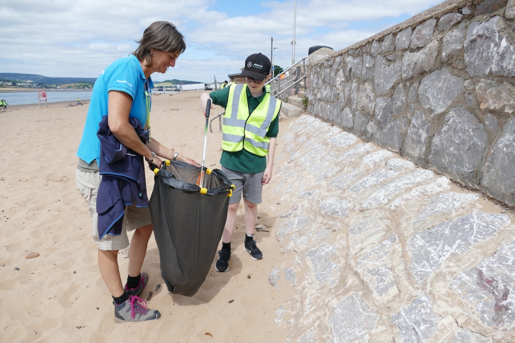 Adult and male children collecting litter on a beach with litter picker and bin bag Adult and male children collecting litter on a beach with litter picker and bin bag