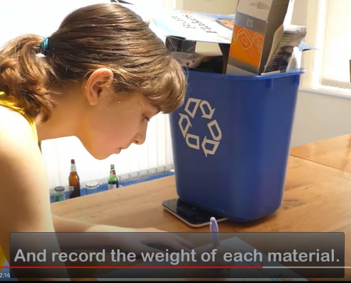 A young girl weighing and recording the weight of cardboard in a blue recycling bin