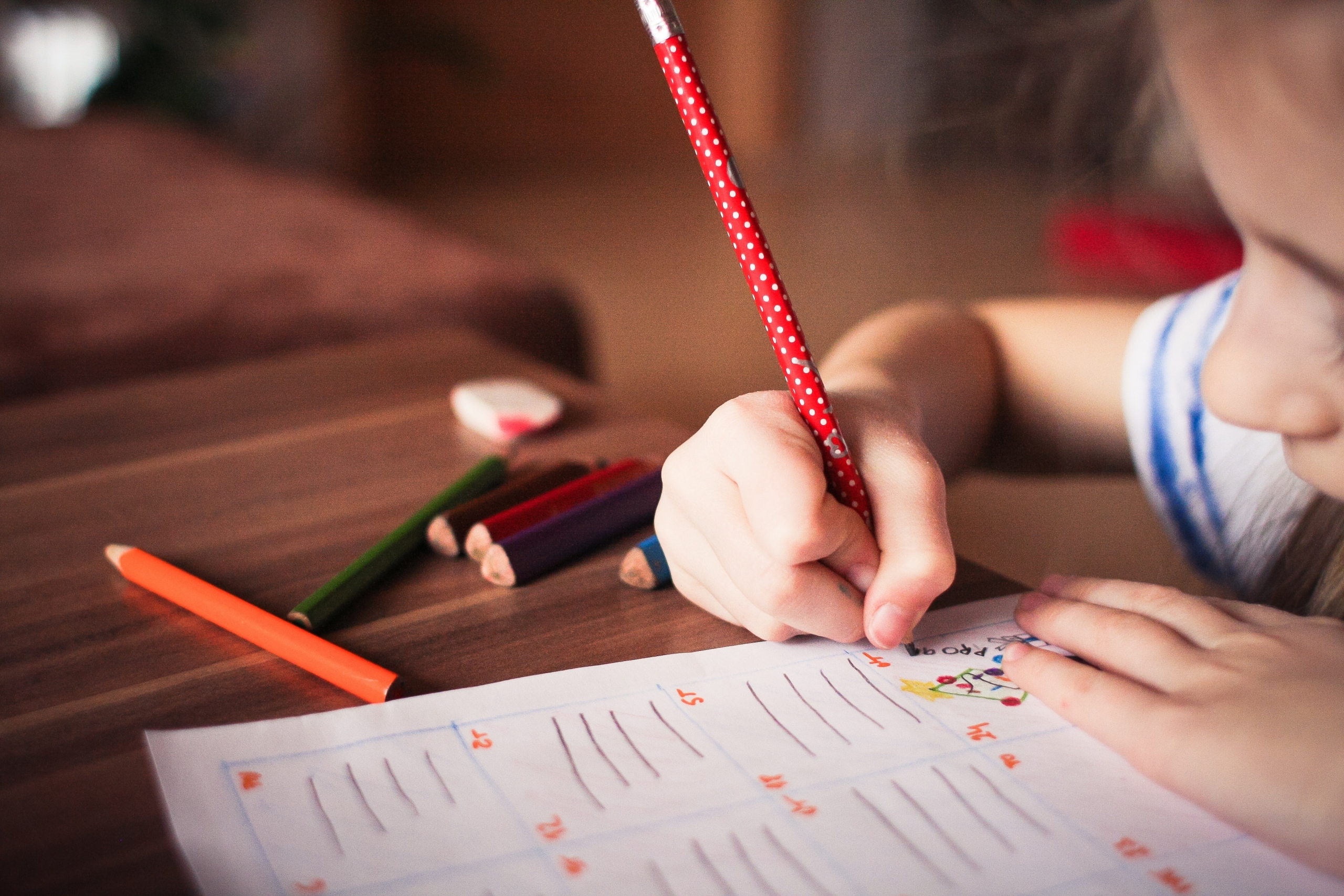 Home & Holiday Activities Close up of child writing on piece of paper, pencil crayons also visible