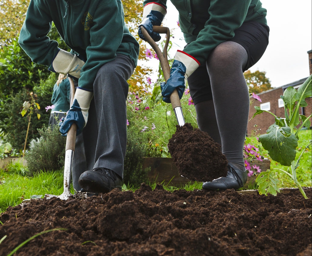 Smiling boy and girl shovelling compost in a school garden