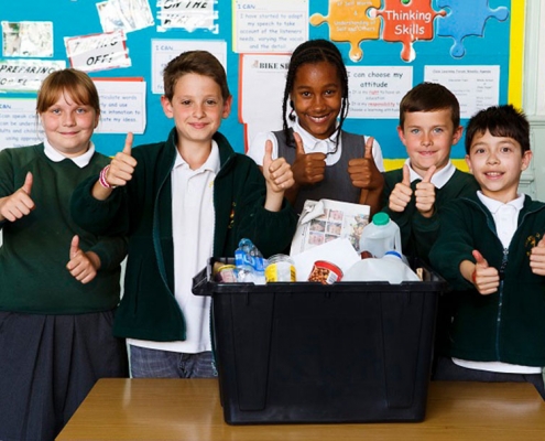 Picture of 5 smiling school children standing behind a recycling box