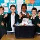 Picture of 5 smiling school children standing behind a recycling box