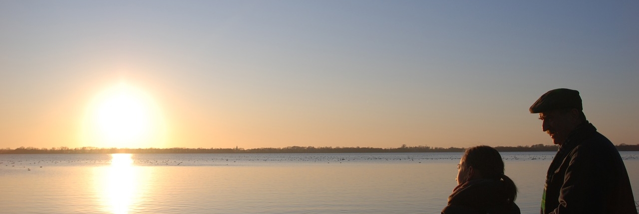 Sustainability Bulletin January 2022 Picture shows a man and child sitting in silhouette watching a winter sunrise over a lake