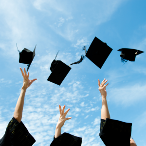 Students throwing graduation hats in the air with a blue sky background