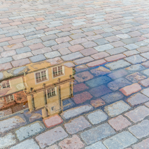 Stone floor pavement with a puddle. The puddle reflects a continental Spanish tall yellow villa