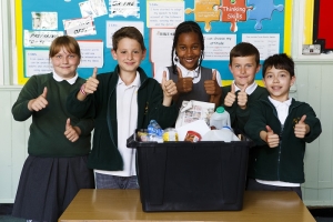 5 smiling children in school uniform standing behind a recycling box full of clean recyclable household packaging