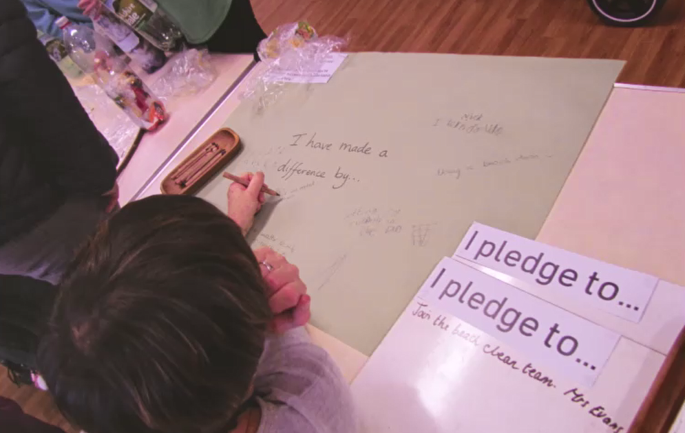 St Peter's Primary School, Budleigh parent writing on a large sheet of paper saying "I have made a difference by..." beside a sign saying I pledge to