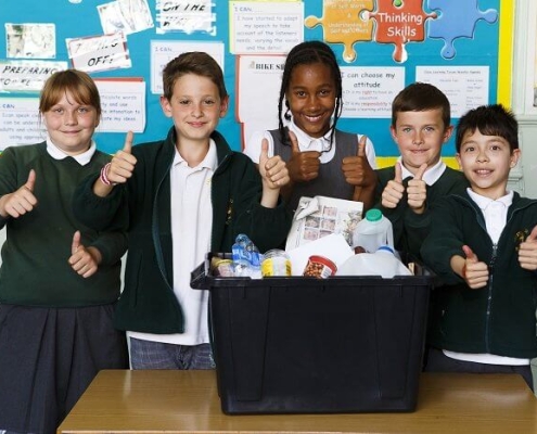 5 smiling children in school uniform standing behind a recycling box full of clean recyclable household packaging